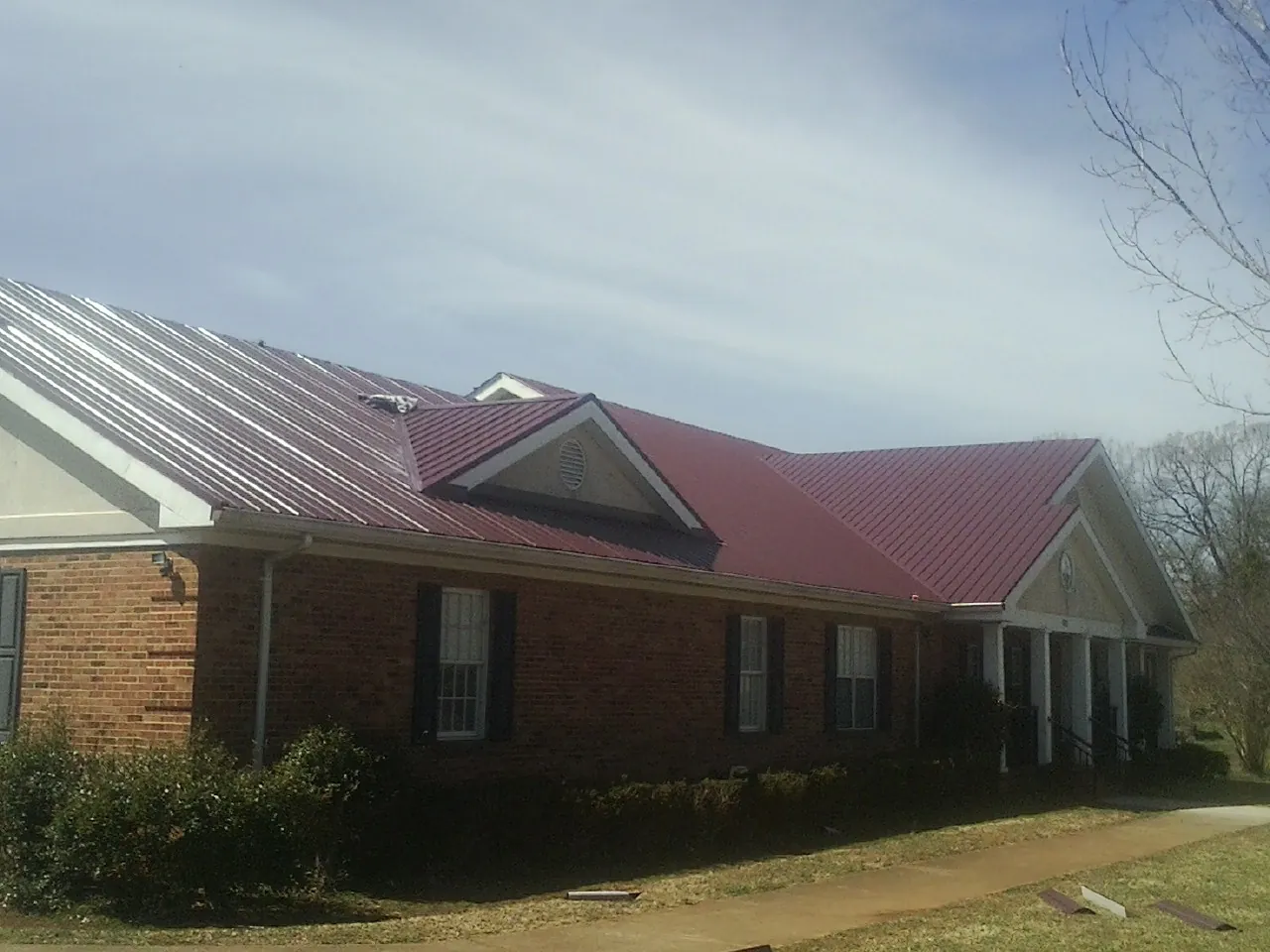 Red metal roof with gabled entries on a long brick building, from a Hail Damage Roof Repair job in Hagerman