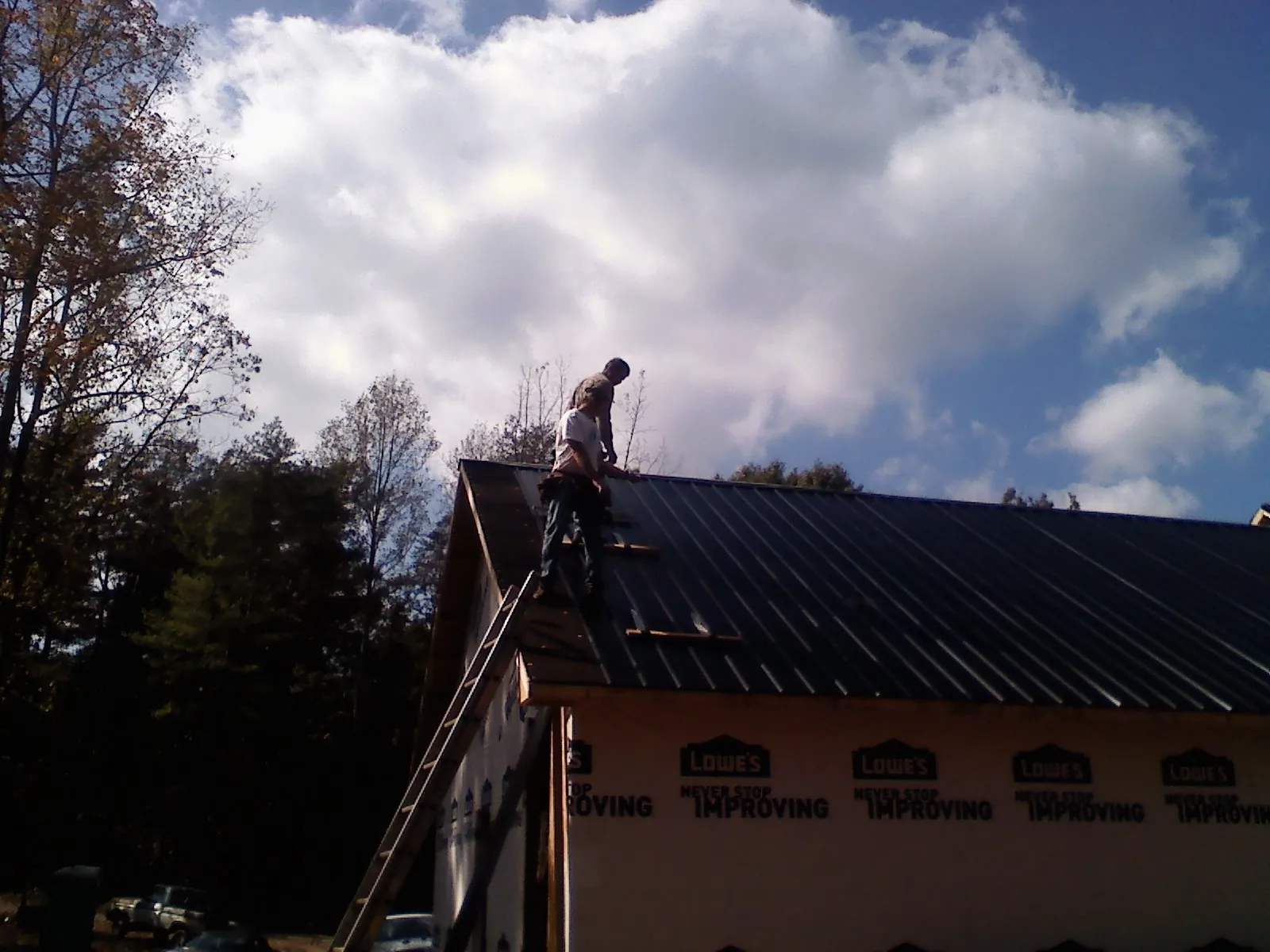Roofer fastening dark metal panels high against a cloudy sky, from a Roof Inspection job in Hagerman
